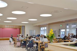 介護施設の共用スペース。入居者と職員が活動している広々としたリビング